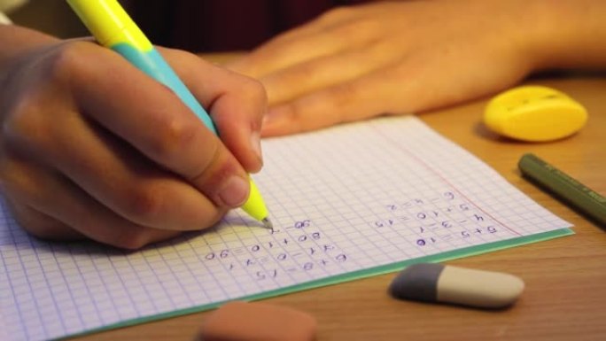 学生的手在笔记本上写数学示例，特写。
