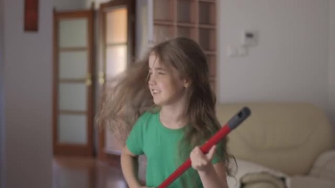 享受清洁俏皮创意儿童舞蹈。富有创造力的少女家庭主妇在家里唱歌时，用扫帚手柄作为吉他的孩子用拖把作为乐