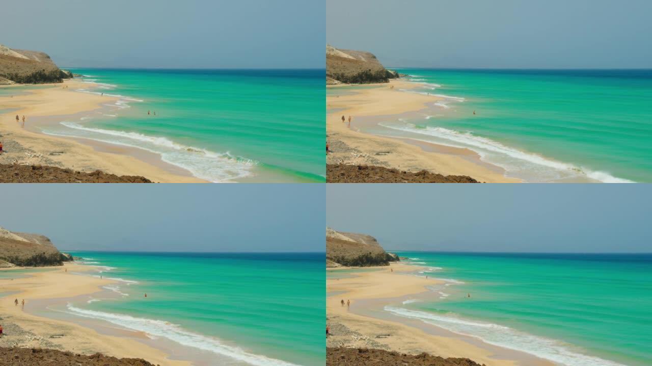 西班牙金丝雀富埃特文图拉岛的碧绿海水海滩。白色沙滩，海洋纹理，泡沫波浪。面目全非的人在岸上放松