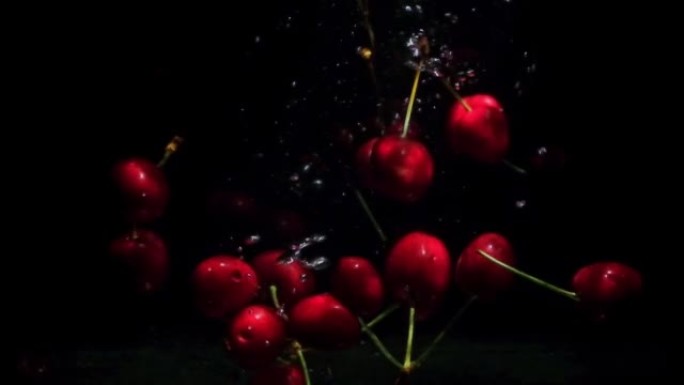 成熟的红樱桃落在水中，黑色背景上有闪亮的气泡。