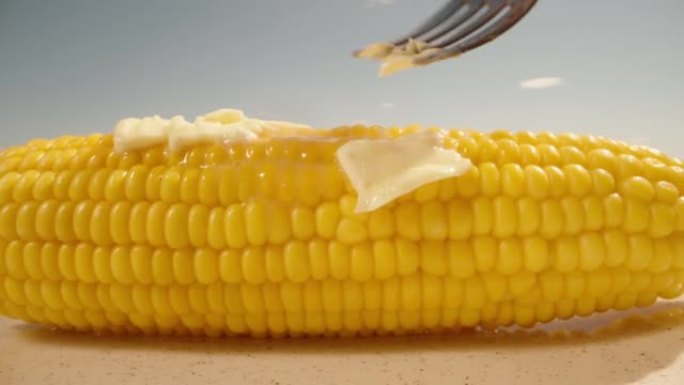 我用叉子把黄油涂在玉米杆上。甜多汁的玉米。夏天，蓝天。特写。宏观。