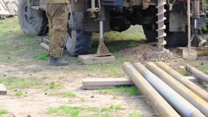 在汽车上安装钻机的工人团队正在钻探自流井以获取地下水。将金属套管插入地面，安装个人饮用水