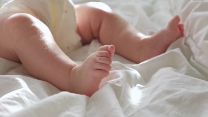 婴儿腿紧贴在白色毯子上。健康的新生脚。温暖的阳光。婴儿小脚在浅色背景上的美丽照片。幼儿发育。真实的坦