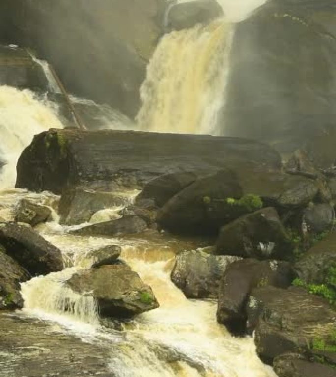 单宁水的框架填充镜头落在长岩石上，并在白水瀑布底部的巨石之间流动