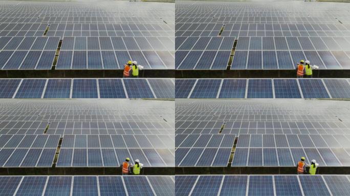 鸟瞰图技术工程师走过太阳能电池板，在太阳能农场检查太阳能电池板。