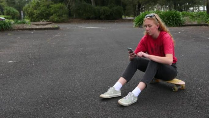 年轻女子坐在滑板上用手机