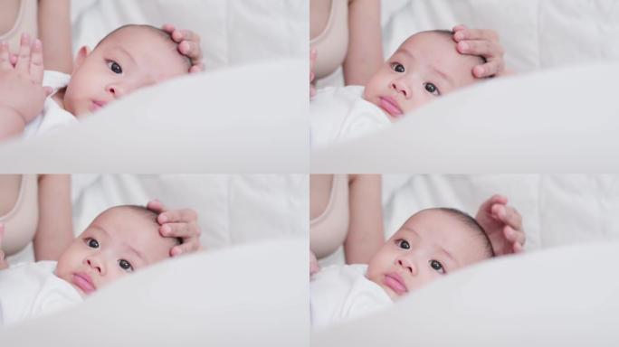脸部特写可爱的亚洲新生婴儿躺在白色床上。当母亲在附近照顾时，家庭时光快乐。天真的小新婴儿可爱。父母身