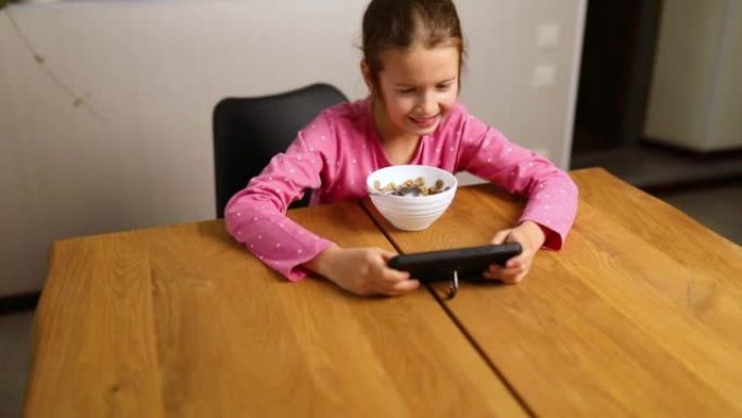 小女孩吃牛奶麦片，在智能手机上玩游戏