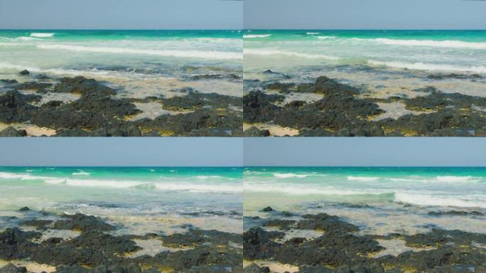 海浪冲过黑色的火山石和白色的沙子。自然，环保，自然奇观概念。透明净化海水。