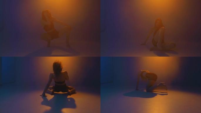 性感的女孩在彩色的灯光下跳舞在烟雾缭绕的工作室。热情的时尚舞蹈在烟雾中。在舞池中表演的女舞者