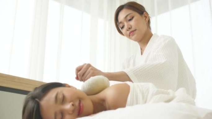 年轻的亚洲女性在水疗沙龙接受泰国草药压缩球背部按摩