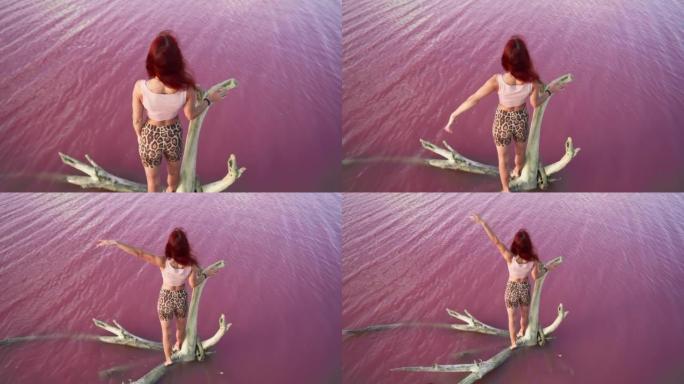 快乐的女人旅行者举起手站在背景美丽的粉红色湖