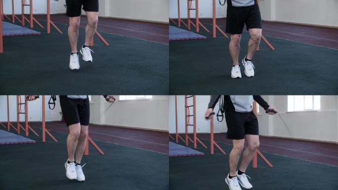 穿着短裤的男人的腿在锻炼前在健身房跳绳。