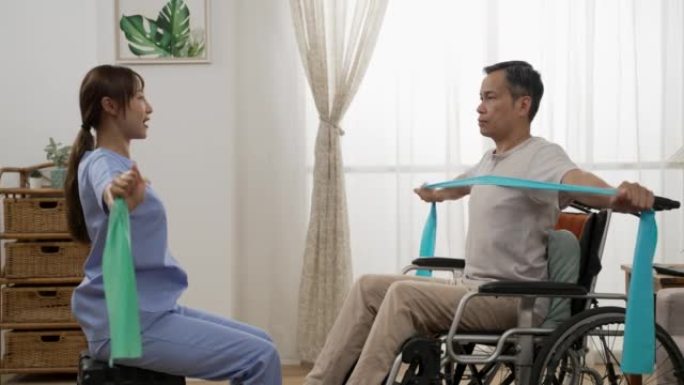 亚洲老年男性轮椅使用者的慢动作在护士的支持下进行理疗阻力训练。他们在家里把弹力带拉在一起