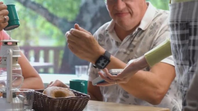 一位老人使用NFC非接触式技术在POS终端上无线使用智能手表支付账单
