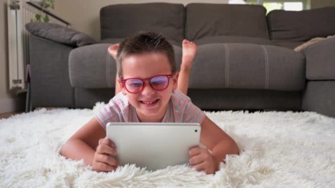 可爱的小男孩在数字平板电脑上看卡通。孩子躺在地板上，用电子设备大笑。儿童室内休闲。高质量4k镜头