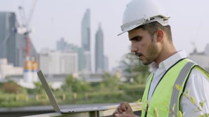 工程师印度的工人使用笔记本电脑检查和站立在具有城市和建筑背景的室外空间。