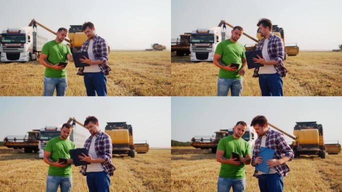 农民站在麦田里，讨论。农艺师，物流代理与触摸平板电脑协商，而收割机将谷物装载到卡车上。用在线数据管理