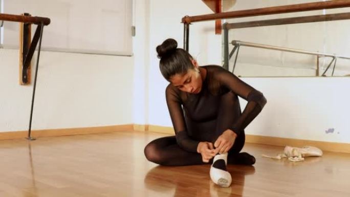 young ballet dancer sitting on the floor lacing up