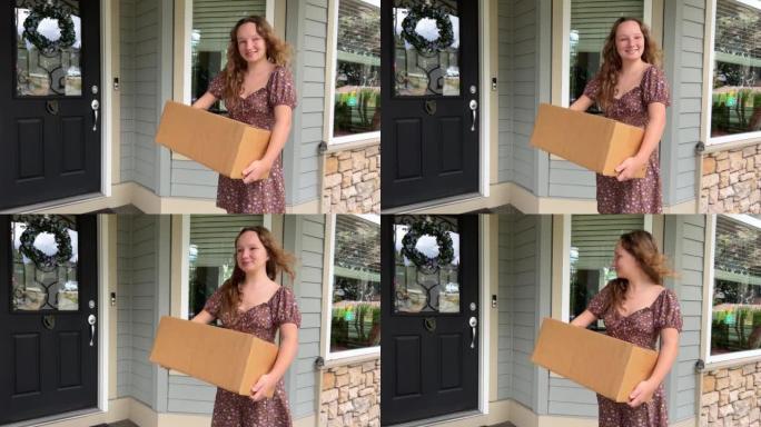 一个女孩站在家门口，手里拿着一个纸箱。她在微笑。她的头发随风飘扬。她穿着一件棕色时尚的夏装短裙。她很