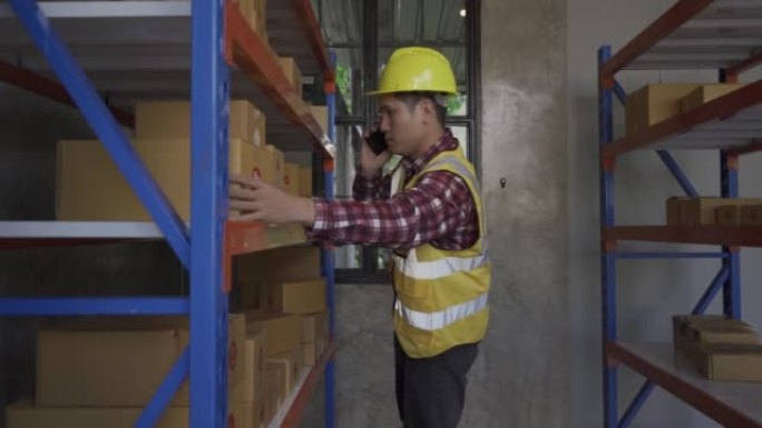 英俊的亚洲员工在仓库工作。穿着高可见度衣服和头盔的工人正在检查和计数货物或箱子以进行交付。中小企业经