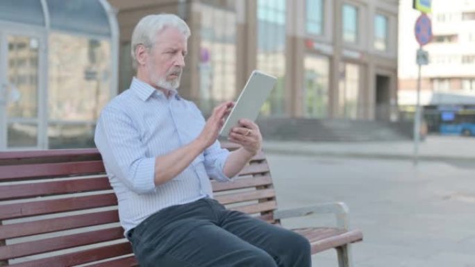 老人坐在户外长凳上使用平板电脑
