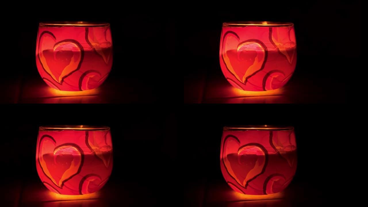 玻璃烛台。在黑色背景上燃烧蜡烛。情人节的浪漫气氛。带有心形图案的装饰性红色粉色蜡烛。侧视图。慢动作。
