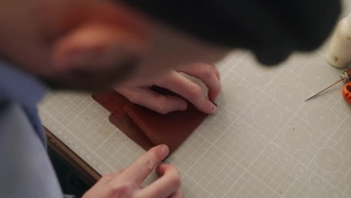 皮革工匠在他的车间工作。制作皮革双折钱包的大师。男人将胶水涂在硬币口袋的形状上，然后粘在一起，然后用