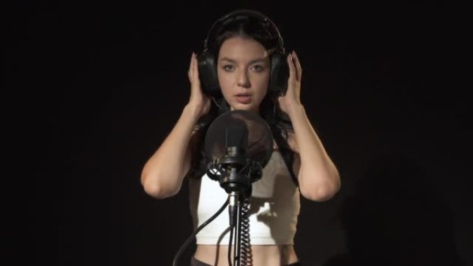 一位情感上有才华的女歌手的肖像戴着耳机唱着悲伤的歌，专业歌手录音。年轻女子在音乐工作室录制歌曲时在黑
