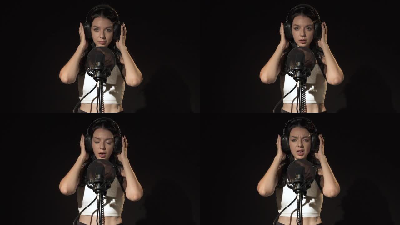 一位情感上有才华的女歌手的肖像戴着耳机唱着悲伤的歌，专业歌手录音。年轻女子在音乐工作室录制歌曲时在黑