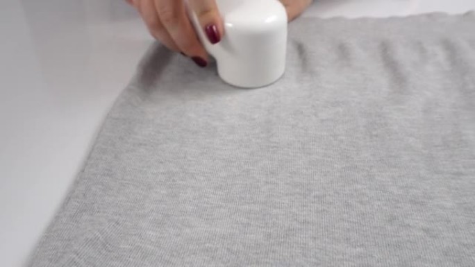 女人用现代手持式电动织物剃须刀去除灰色毛衣上的起球。衣服护理概念。