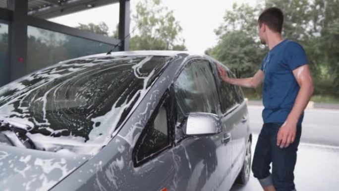 自助洗车场的一男一女。快乐的夫妇在阳光明媚的日子洗车，在院子里玩得开心。女孩和男孩在压力下用泡沫和水