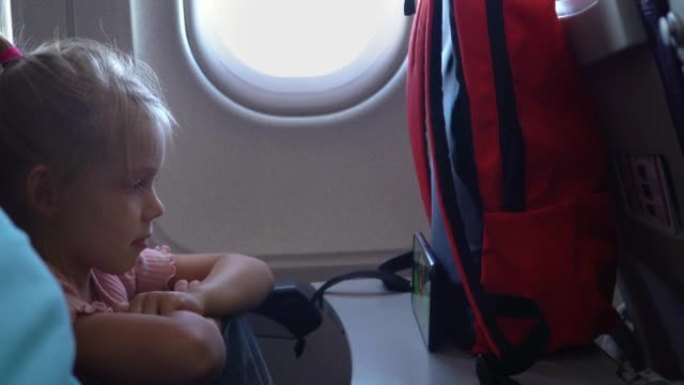 带着手机的小孩坐在飞机上的照明器旁，看动画片。旅行、度假、旅行的概念。运输