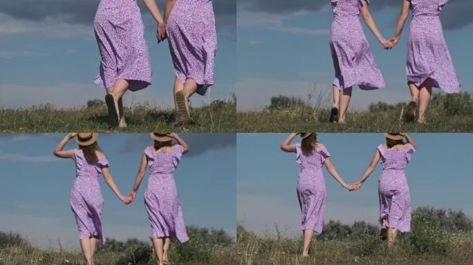 穿着紫色夏装的年轻双胞胎姐妹手牵着手走在绿色的田野里