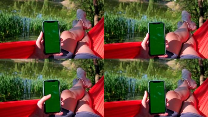 女人的观点在躺在吊床上时用绿屏刷手机