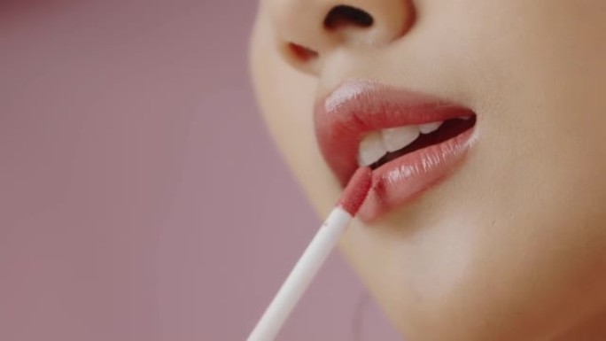 特写年轻的亚洲女性在粉红色背景上孤立的嘴唇上涂抹口红，慢动作拍摄。