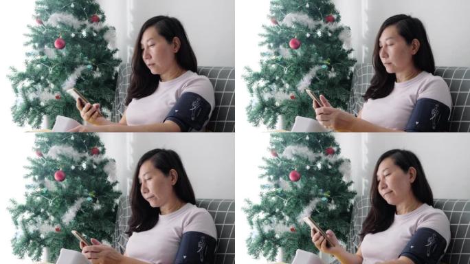 亚洲成年女性坐在家里圣诞树附近的沙发上，与医生交谈，进行血压测试，生活方式概念。