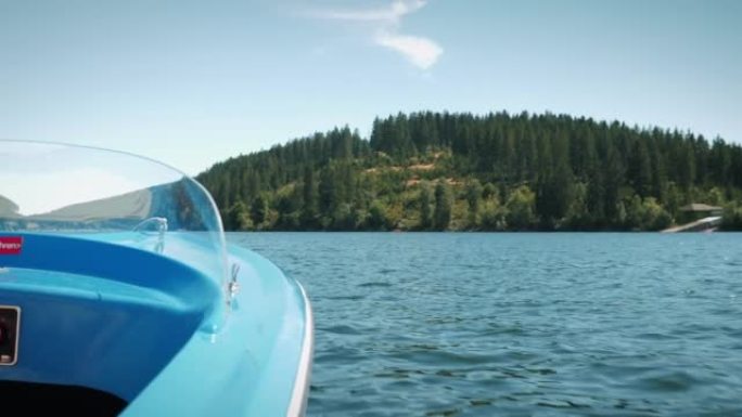 在山湖上航行的电动船。蓝色旅游船漂浮在湖边的水上，背景是绿树和山丘。夏季邮轮假期。航海和旅行概念