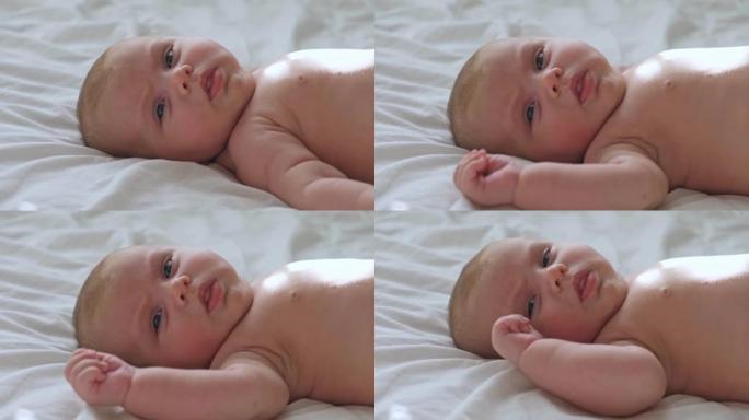 白色毯子上新生婴儿的特写肖像。软聚焦。婴儿在撒谎，打哈欠。一，两周大。女婴在家床上醒来。新生活和成长