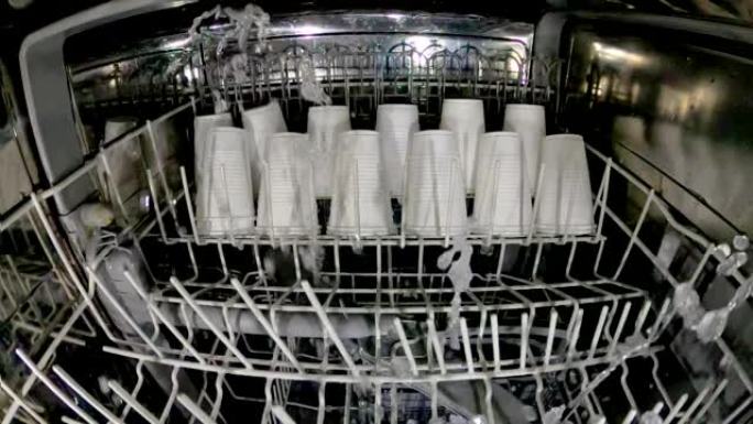 塑料盘子在洗碗机中清洗。疯狂的想法是在洗碗机里洗塑料眼镜。查看洗碗机和塑料一次性餐具。慢动作内部视图