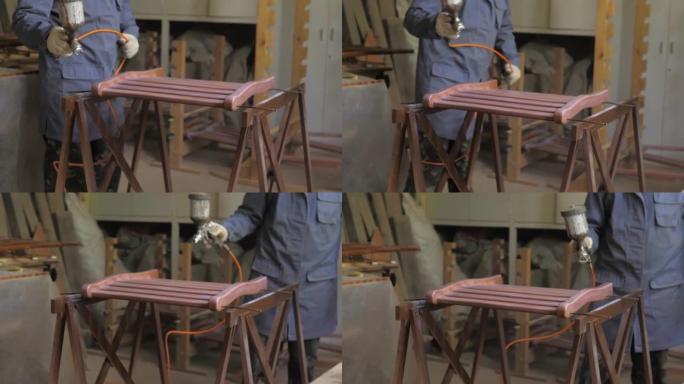慢动作。木匠-戴着手套的人，在木质表面上涂上清漆或压缩空气底漆。在一家家具厂的木工车间用喷枪绘画木制