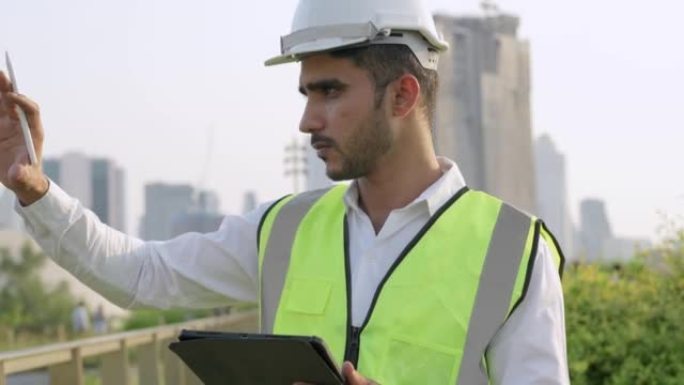 印度工程师的工人介绍了带有智能平板电脑的项目，以检查和站立在具有城市和建筑背景的室外空间。