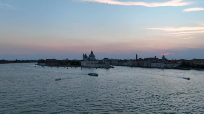 圣玛丽亚德拉致敬罗马天主教堂和小教堂的空中无人机日出场景，大运河和朱德卡运河之间的交通船位于意大利威