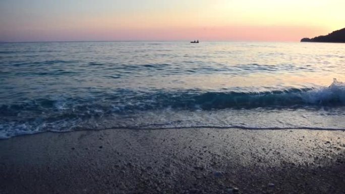 平静的海面在前景中冲浪，一艘小船和两个渔民在粉红色的日落天空中冲浪。