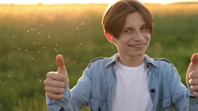 积极的青少年男子微笑着对着镜头，并在日落时在户外展示拇指。青春与积极情感观念