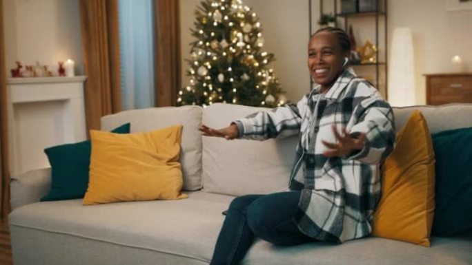 冬天的晚上。圣诞树闪烁。一名非洲裔学生坐在客厅的沙发上，戴着耳机听最喜欢的歌曲。她随着歌曲的节奏和微