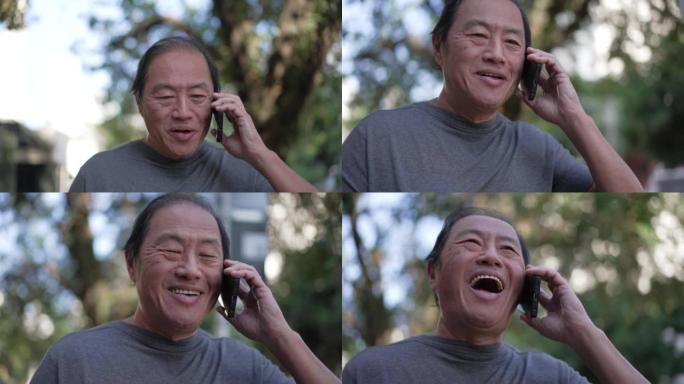 快乐的亚洲高级男子在城市街道上行走时打电话。一个中年老人与手机设备交谈的肖像