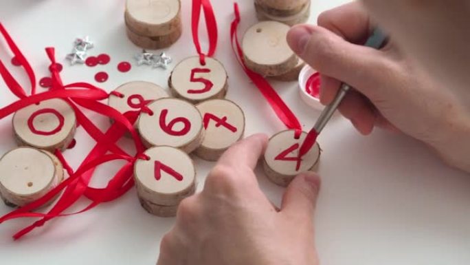画，为圣诞节和新年的孩子们制作一个降临日历。女人的手拿着毛笔，写一个数字。日历日。装饰用木制坯料。侧
