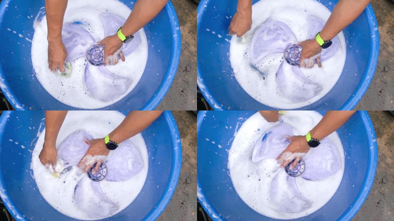 一个男人的手在一个充满白色气泡的蓝色浴缸里洗风扇叶片。