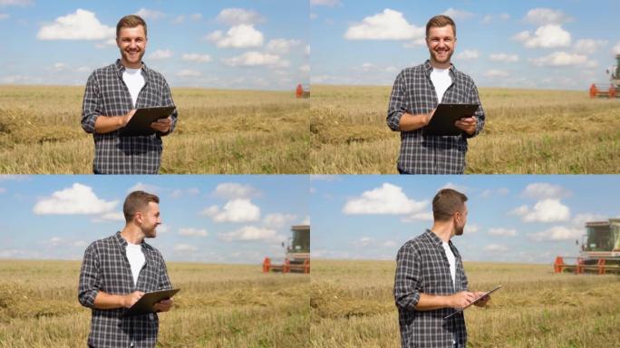 快乐的年轻农民，笔记本站在麦田上，联合收割机在后台工作